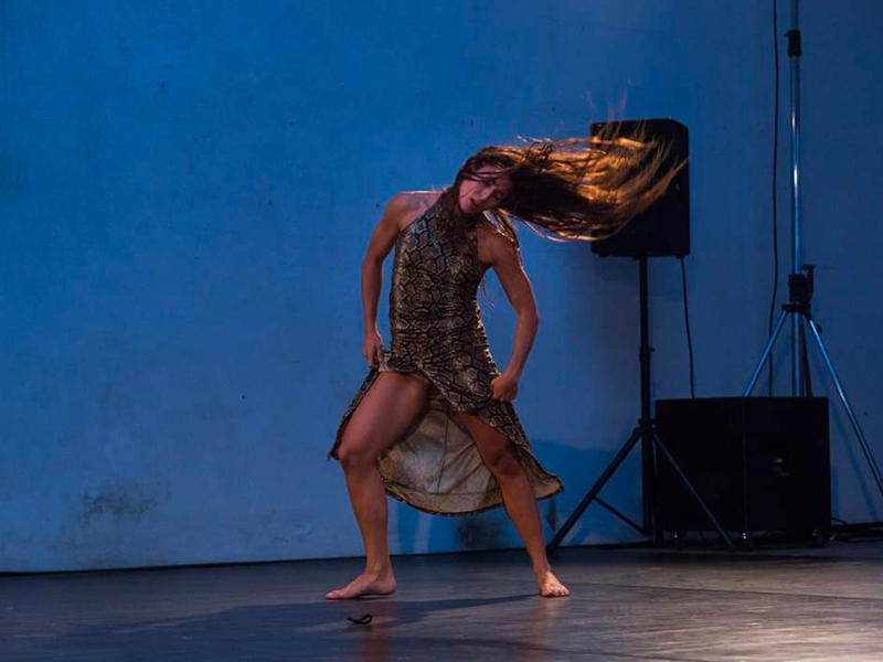 la danzatrice è immortalata mentre danza, la posizione è frontale. La luce nella sala ha una tonalità tendente al blu.