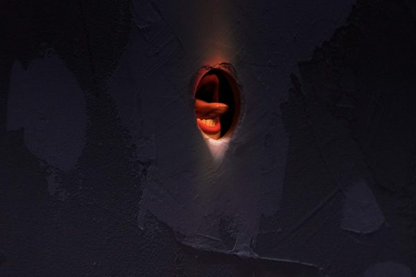 una bocca con labbra rosse esce da un muro bianco