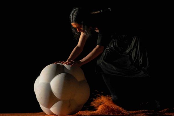 un danzatore spinge una sfera di pietra bianca