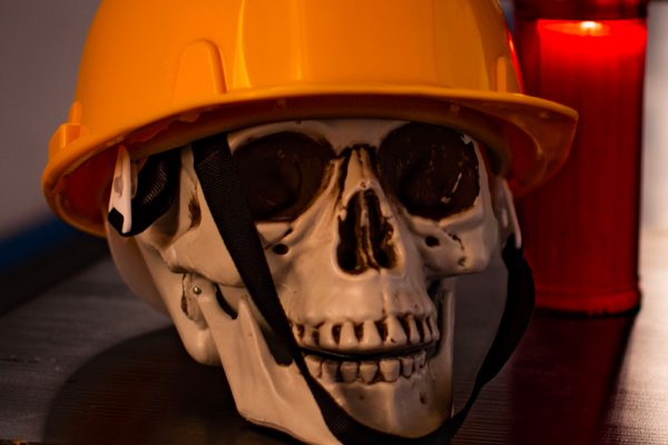 un finto cranio umano che “indossa” un casco giallo da cantiere. Al suo fianco è acceso un lumino votivo di colore rosso.
